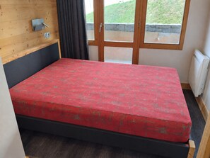 Ein Zimmer mit einem Bett, einer Holzwand, einem Fenster mit Ausblick und einer Heizung.