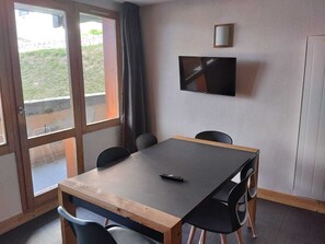 Ein Zimmer mit einem Holztisch, vier Stühlen, einem Fernseher an der Wand und einer Glastür, die nach draußen führt.