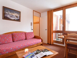 A cozy room with a wooden sofa, a small table with a candle and magazines, a wooden chair, and a large window with curtains. - Apartment near slopes with balcony (Plagne Bellecôte)