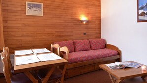Une pièce chaleureuse avec un mur en bois, un canapé, une table à manger avec des chaises et une petite table sur laquelle se trouvent une bougie et des magazines.