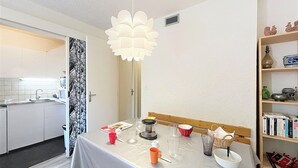 A dining area with a table set for two, a hanging light fixture, and a bookshelf with books and decorative items. - Studio 4/5 pers. Ski-in, Balcony, Pets Allowed (Le Corbier)