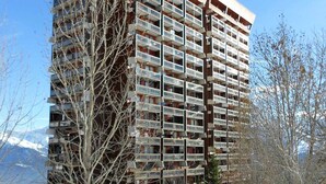 A multi-story building with numerous balconies, surrounded by bare trees and a snowy landscape. - Studio 4/5 pers. Ski-in, Balcony, Pets Allowed (Le Corbier)
