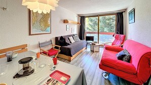 A modern hotel room with a bed, a red sofa, a dining table with a coffee maker, and large windows offering a view of trees. - Studio 4/5 pers. Ski-in, Balcony, Pets Allowed (Le Corbier)