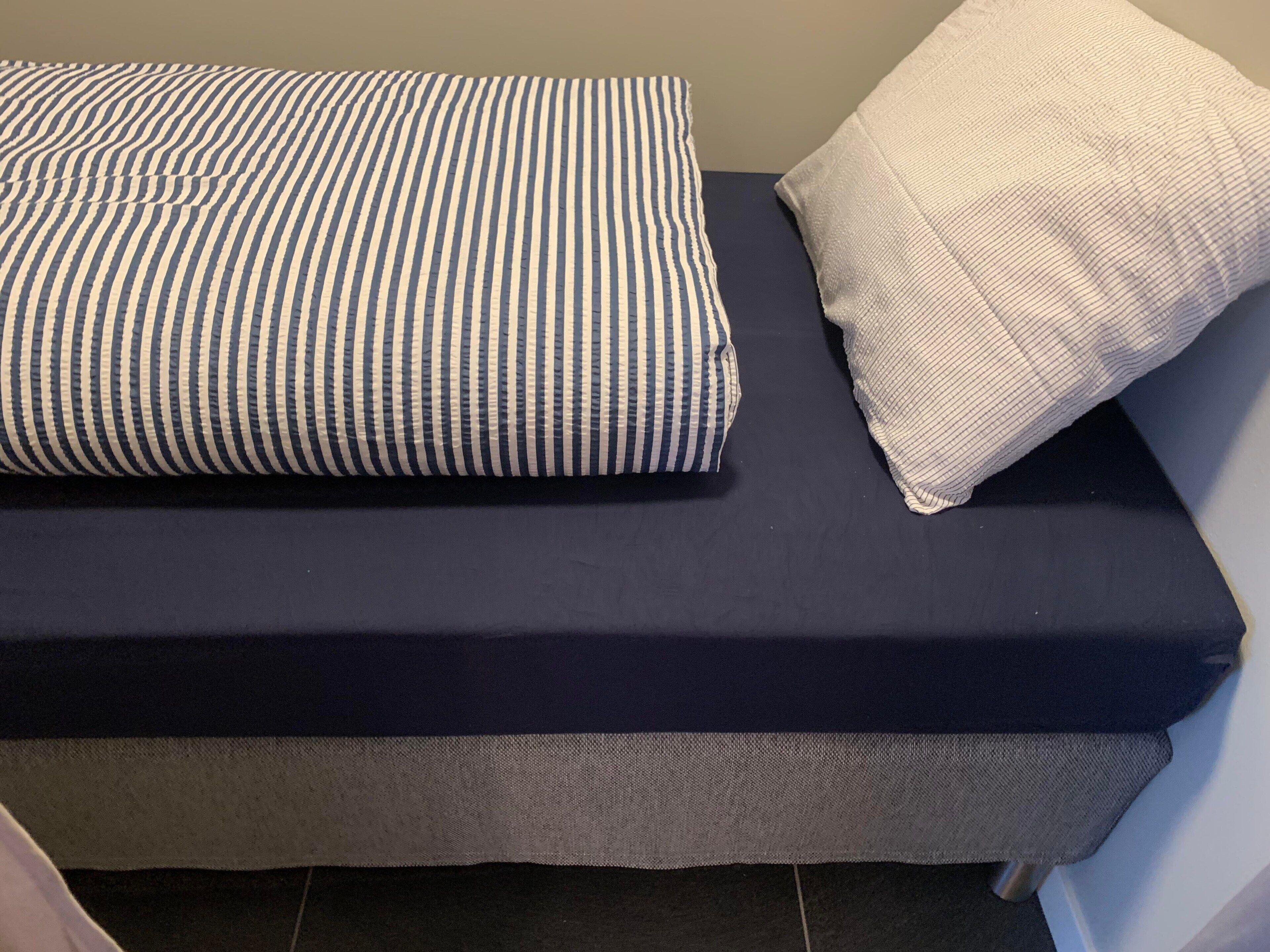 A bed with a dark blue mattress and two pillows, one striped and one plain.