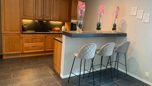 A kitchen with wooden cabinets, a granite countertop, and a bar area with four bar stools. - Notodden Sentrum Apartment NO 8 (Notodden)