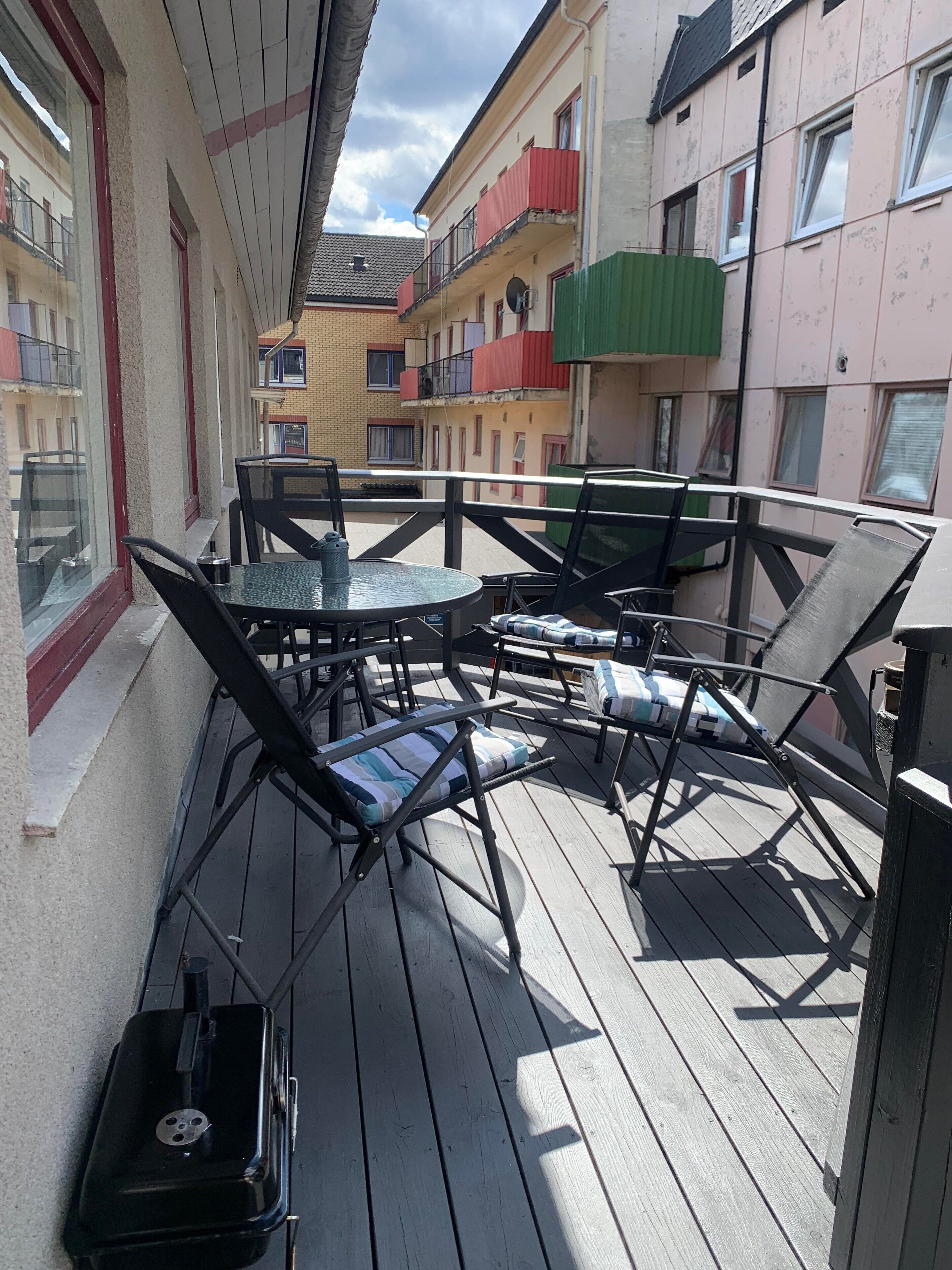 A balcony with a round table and chairs, a suitcase, and a view of adjacent buildings with balconies.