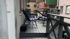 A wooden deck with a doormat, outdoor furniture, and a view of neighboring buildings. - Notodden Sentrum Apartment NO 8 (Notodden)