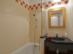 Casa de banho com banheira, chuveiro com divisória de vidro, lavatório com espelho e toalha sobre o lavatório.