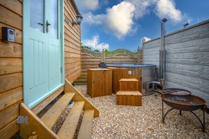A wooden cabin with a turquoise door, a hot tub, and a barbecue grill. - Rosemary - 1 Bedroom - Amroth (Narberth)
