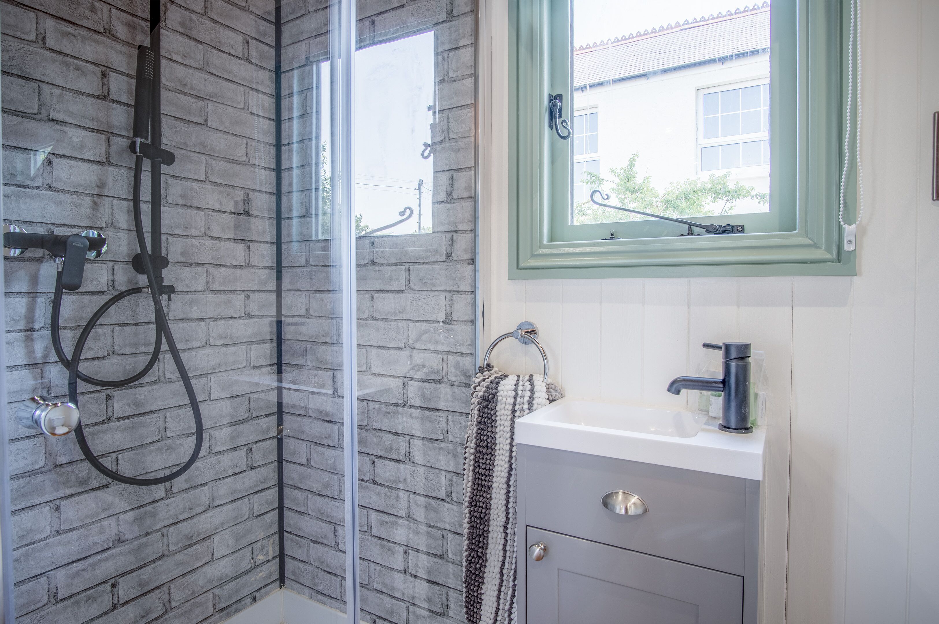 A bathroom with a glass shower enclosure, a white sink, and a window with a green frame.