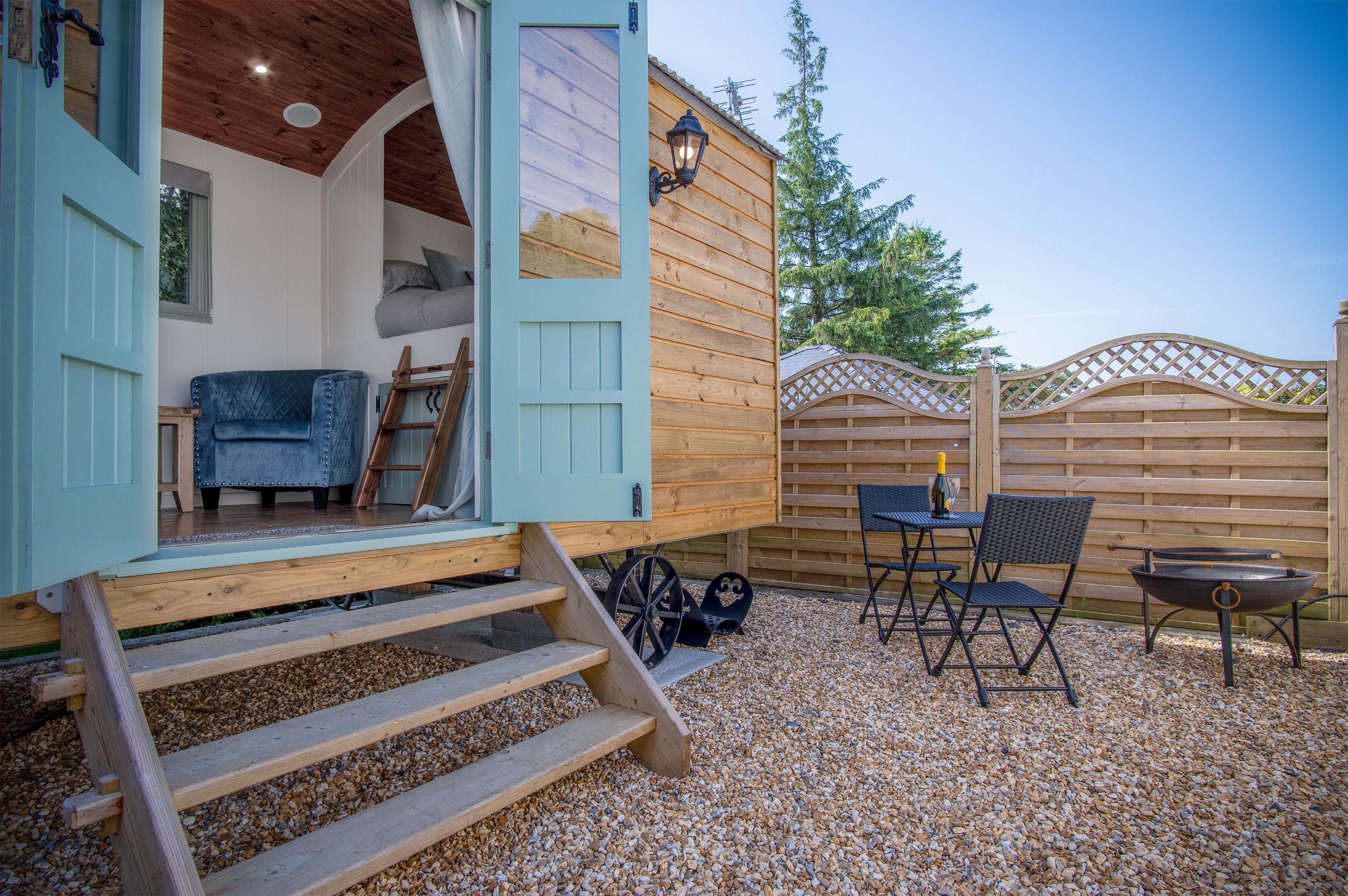 Un espace extérieur accueillant avec une terrasse en bois, une porte bleue donnant accès à un espace intérieur, une table avec des chaises et un foyer.