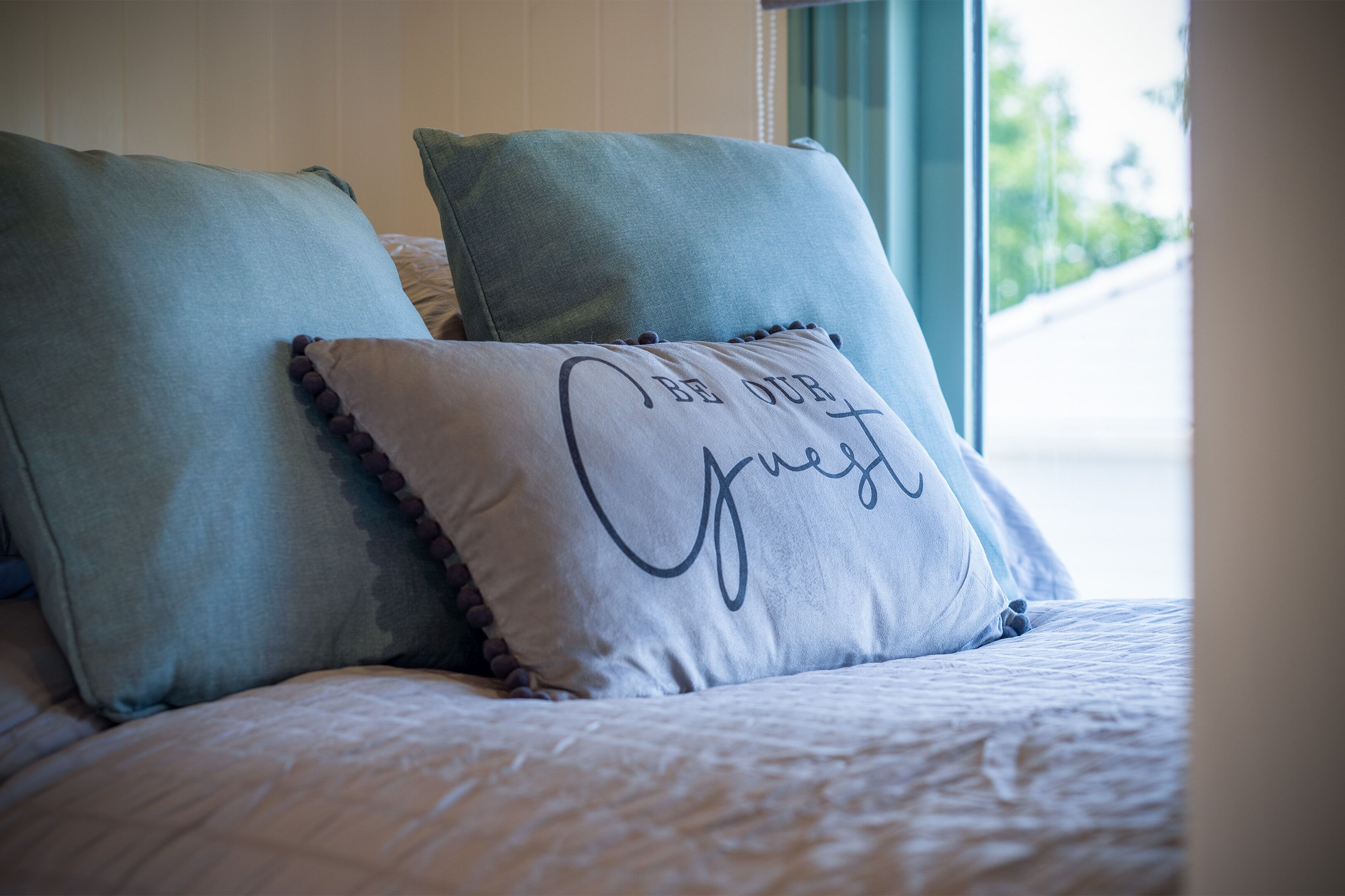 A bed with two pillows and a decorative pillow with text.