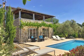 Ein zweistöckiges Steinhaus mit Swimmingpool, Sitzgelegenheiten im Freien und einer mit Wein bewachsenen Pergola.