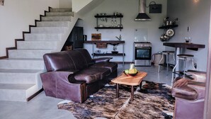 Un salon moderne avec un canapé en cuir, une table basse en bois et un escalier menant à un niveau supérieur.