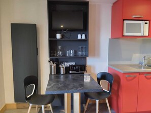 A compact kitchen with a dark countertop, two black chairs, a microwave, and a shelf with glassware and utensils. - Renovated studio for 2, ski-in, pets, parking (La Plagne Montchavin Les Coches)