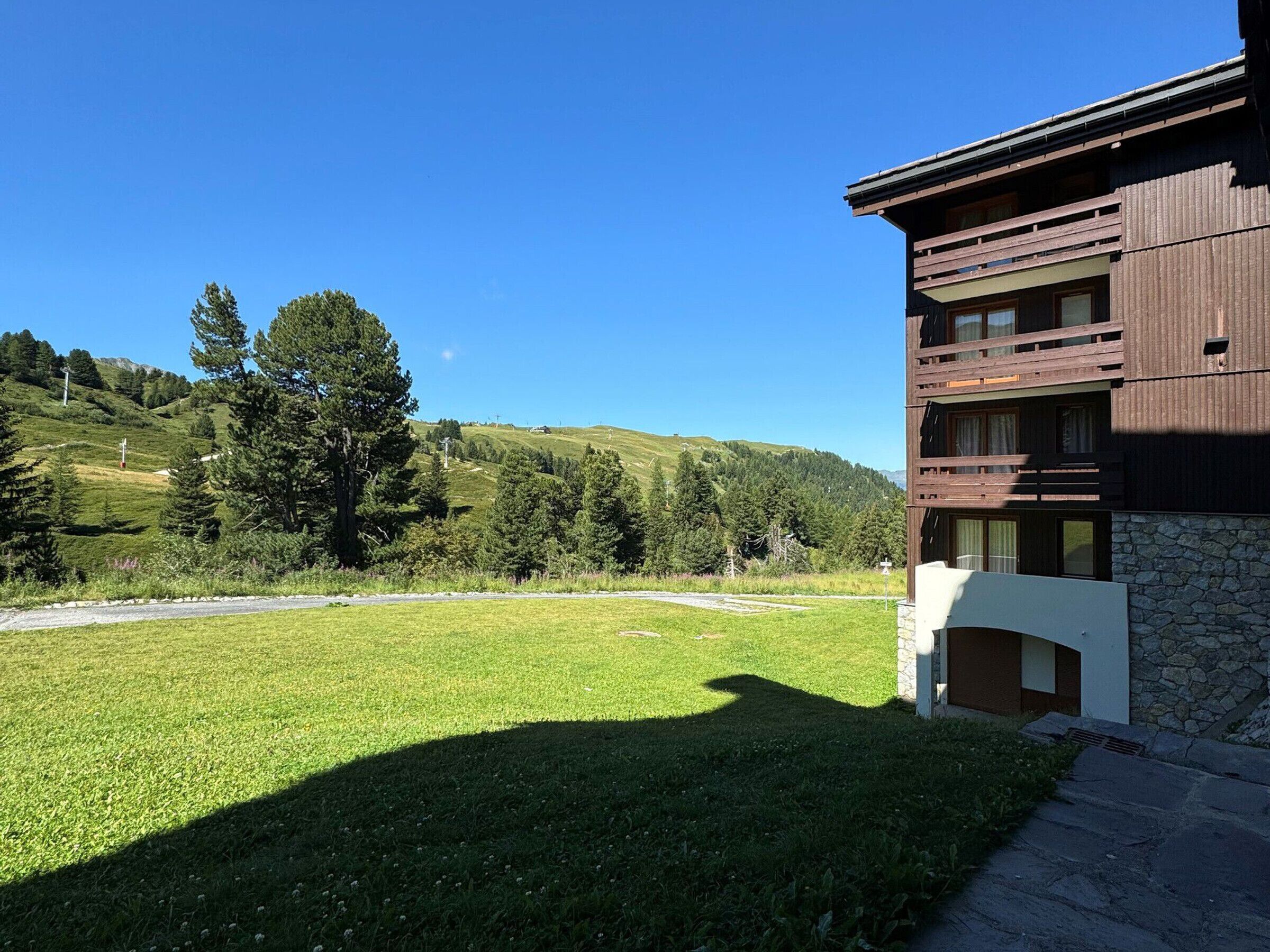 A modern building with a stone facade and wooden balconies, set against a backdrop of green hills and trees.