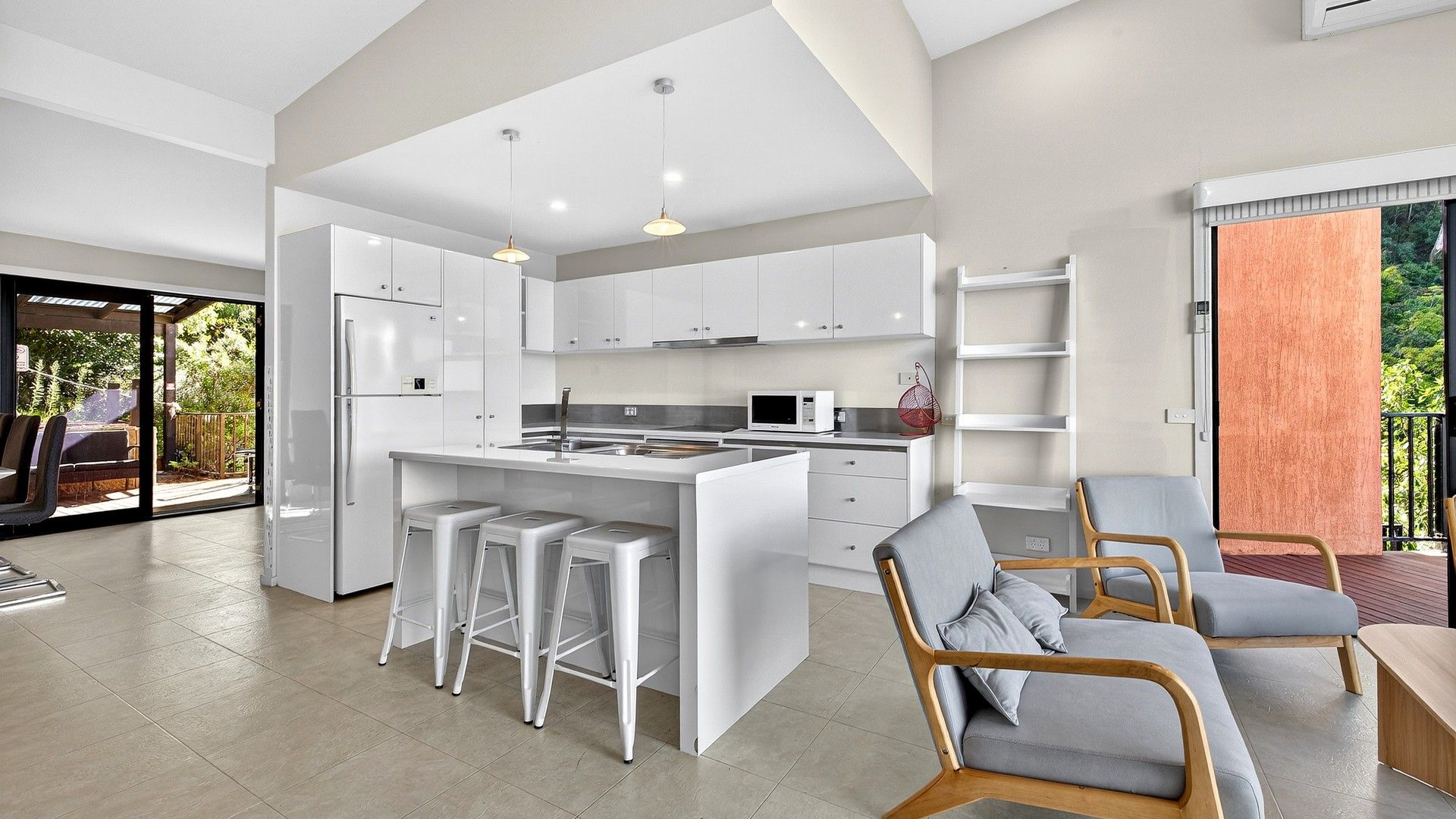 Une cuisine moderne avec des meubles blancs, un îlot central doté de tabourets et un coin repas avec une table et des chaises en bois.