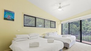 Ein Schlafzimmer mit zwei Betten, einem Deckenventilator und großen Fenstern mit Jalousien.