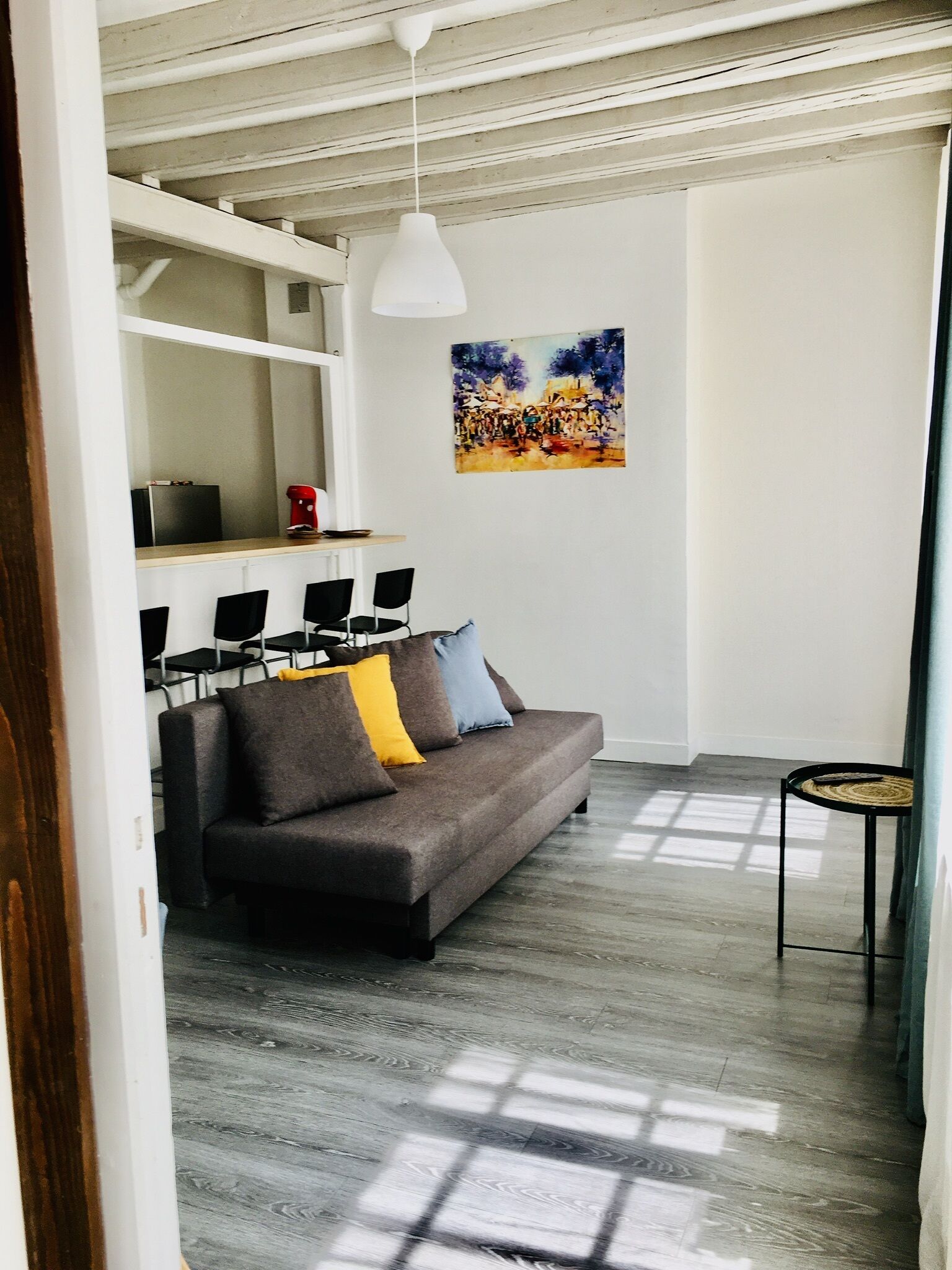 A modern living room with a grey sofa, black chairs, a small round table, and a painting on the wall.
