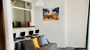 Ein modernes Wohnzimmer mit einem grauen Sofa, schwarzen Sesseln, einem kleinen runden Tisch und einem Gemälde an der Wand.