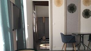 Ein modernes Wohnzimmer mit einer grauen Couch, einem kleinen runden Tisch und zwei blauen Sesseln. An der Wand ist ein Flachbildfernseher angebracht und ein dekoratives Wandbild zu sehen.