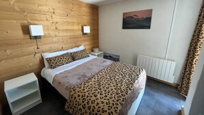 Une chambre d’hôtel avec une tête de lit en bois, un lit recouvert d’une courtepointe à motifs léopard, deux tables de chevet avec des lampes, un radiateur et un tableau accroché au mur.