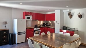 Une cuisine moderne avec des meubles de rangement rouges, un réfrigérateur blanc et une table à manger en bois, assortie de chaises blanches.