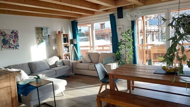 En hyggelig stue med træloft, sofa, spisebord og reol.