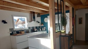 Et moderne køkken med hvide skabe, træloft og udsigt til et hus gennem et vindue.