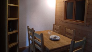 A wooden dining table with four chairs, a window with wooden framing, and a shelf unit with a few items on it. - Bright divisible studio, direct piste access, balcony, pets allowed (Plagne Bellecôte)