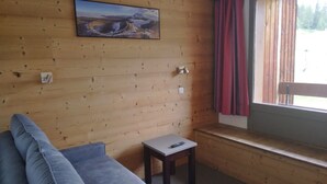 A wooden-paneled room with a sofa, a small table, and a window with curtains. - Bright divisible studio, direct piste access, balcony, pets allowed (Plagne Bellecôte)