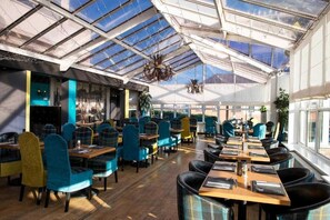 A restaurant with a high ceiling and skylights, featuring tables and chairs with a plaid pattern upholstery. - Avonbridge Hotel (Hamilton)