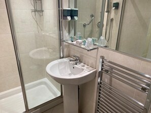 A modern bathroom with a glass shower enclosure, a pedestal sink, and a towel rack. - Avonbridge Hotel (Hamilton)