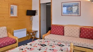 A cozy room with a wooden wall, a sofa with patterned cushions, a small table, a mounted television, and a framed picture on the wall.