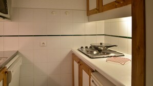 A kitchen with white tiles, a stove, and wooden cabinets.