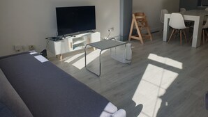 Una sala de estar moderna con un televisor de pantalla plana, una mesa de comedor con sillas y un taburete de madera.