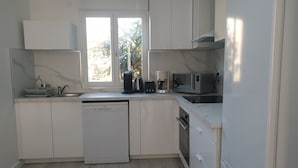 Una cocina moderna con armarios blancos, lavavajillas, cafetera, microondas y refrigerador.