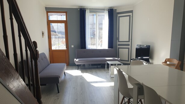 Una sala de estar moderna con un sofá, una mesa de comedor con sillas, un televisor y una escalera.