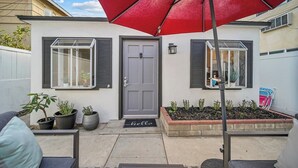 A residential house with a grey door, two windows with shutters, a red umbrella, and a small garden area with plants. - Two Bedroom Beach Cottage in Pacific Beach, San Diego (San Diego)