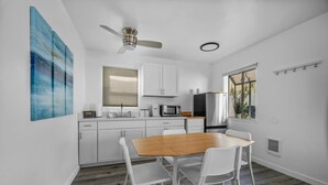A modern kitchen with white cabinets, a wooden dining table, and a ceiling fan. - Two Bedroom Beach Cottage in Pacific Beach, San Diego (San Diego)