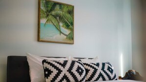 A bed with white and black patterned pillows, a dark headboard, and a painting of a palm tree on the wall. - Two Bedroom Beach Cottage in Pacific Beach, San Diego (San Diego)