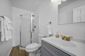 A modern bathroom with a glass shower enclosure, a white toilet, a vanity with a sink, and a mirror above the mirror. - Studio Beach Rental in Pacific Beach, San Diego (San Diego)