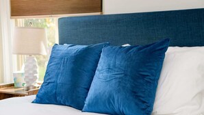 Een bed met twee blauwe kussens en een wit kussen, een houten hoofdbord en een lamp op een nachtkastje.