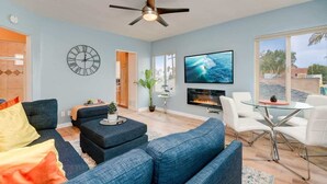 Een woonkamer met blauwe banken, een televisie, een open haard en een plafondventilator.