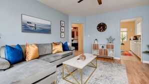 A living room with a grey sofa, a coffee table, a ceiling fan, and a clock on the wall. - Beach & Park Family Fun Getaway -Steps to Sand (San Diego)