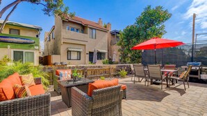 An outdoor patio area with wicker furniture, a red umbrella, and a grill. - Beach & Park Family Fun Getaway -Steps to Sand (San Diego)