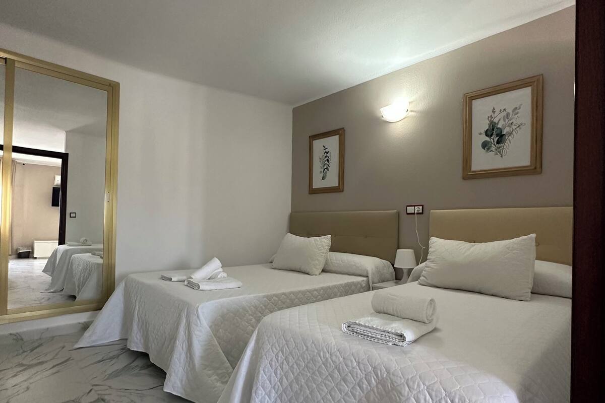 A hotel room with two beds, a large mirror, and artwork on the walls.
