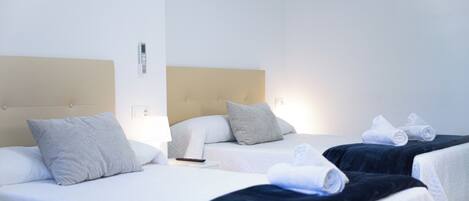 A hotel room with two beds, each with a headboard, pillows, and a remote control on the nightstand.