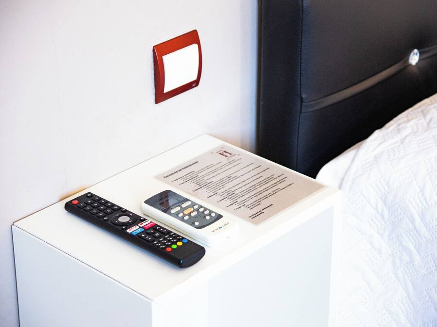 A bed with a white comforter and a remote control on a white bedside table.