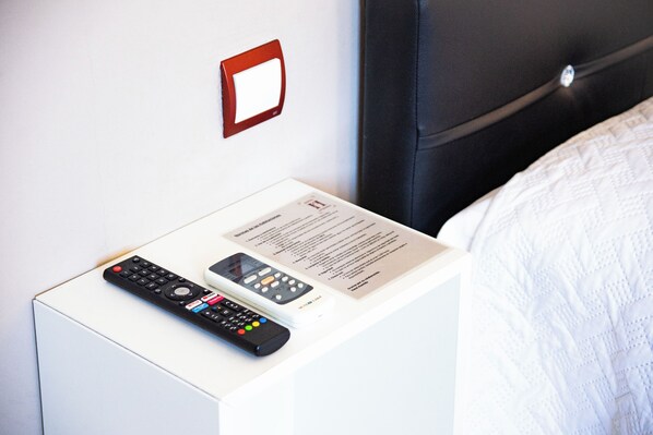Un lit avec une couette blanche et une télécommande posée sur une table de chevet blanche.